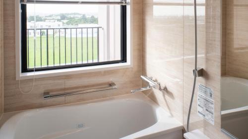 a bathroom with a bath tub and a window at REF Okinawa Arena by VESSEL HOTELS in Okinawa City