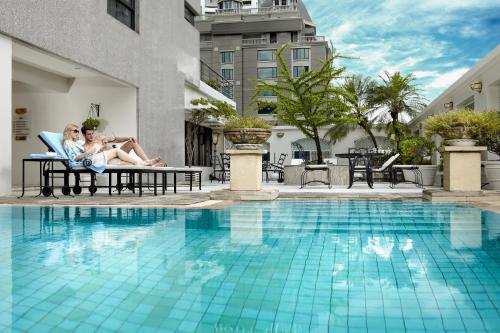 twee personen in stoelen naast een zwembad bij Cape House Langsuan Hotel in Bangkok