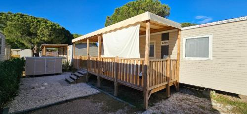 a wooden cabin with a deck next to a building at Kokua Développement présente MOBIL HOME résidentiel toutes options camping 4 étoiles CANET in Canet-en-Roussillon