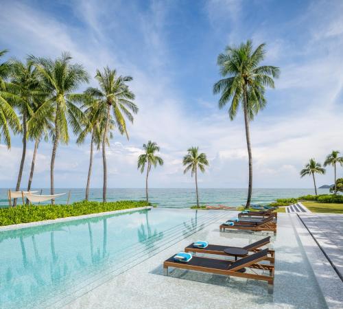 - une piscine avec des chaises longues et des palmiers dans l'établissement Centara Reserve Samui - SHA Plus, à Chaweng