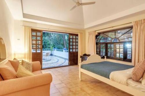 a bedroom with a bed and a couch and a window at Riveranda · 4bhk villa with private pool in Goa