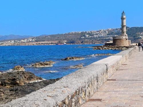 a stone wall next to the water with a lighthouse at Sofias Home in Chania