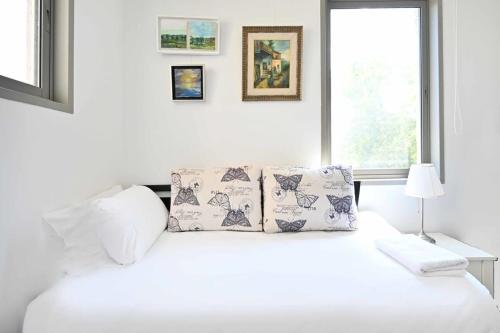 a white bedroom with a bed with pillows and a window at Smiling Joe by HolyGuest in Tel Aviv