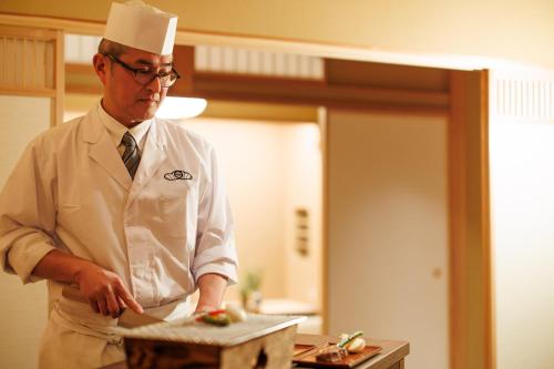 a man in a chefs hat preparing food in a kitchen at Shoraiso in Yamanouchi
