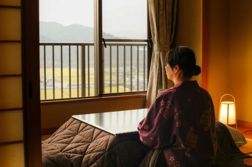 Eine Frau, die auf einem Bett sitzt und aus dem Fenster schaut. in der Unterkunft Yumenoi in Himeji