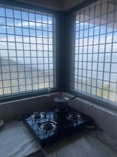 a stove with a pot on it in a kitchen with windows at Maayaa Ridge House in Kanatal