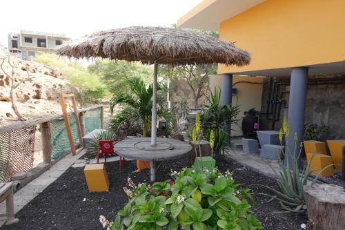 un patio con una mesa y una sombrilla de paja en Residencial Ribeira Torta, en Porto Novo