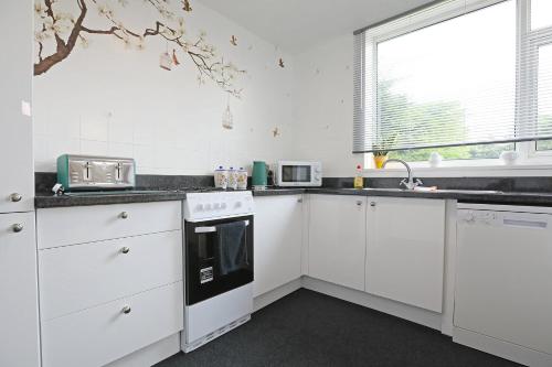 a white kitchen with white cabinets and a window at Lovely 3 bedroom house with free parking & garden in Norwich