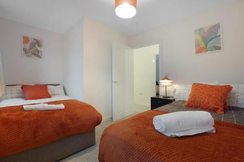 a bedroom with two beds with orange and white sheets at Gravesend 2 Bed Apartment-2 minutes walk from shops, Restaurants and Motorway. Sleep upto 5 in Northfleet