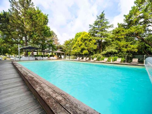 une grande piscine avec des chaises et des arbres dans l'établissement Mercure Bordeaux Lac, à Bordeaux