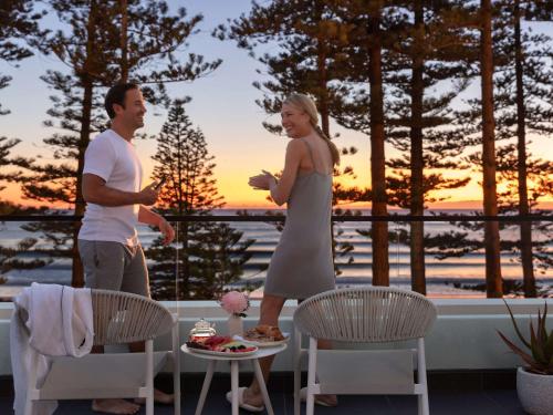 Un uomo e una donna in piedi su un patio con un tramonto di Manly Pacific Sydney MGallery Collection a Sydney