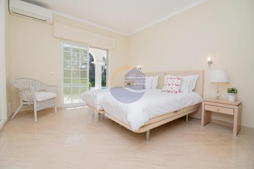 a white bedroom with a large bed and a chair at Villa Luxury Suites, Heated Outdoor Pool in Portimão