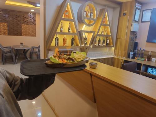 una persona sosteniendo una bandeja con un plato de comida en un mostrador en Hotel OM, en Baudhatinchule