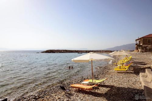 a beach with chairs and umbrellas and the water at Waveside Sanctuary - Luxurious Seastone Villa in Avia