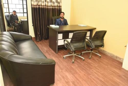 a man sitting at a desk in an office with chairs at Hotel GRG Varanasi Paradise Varanasi in Varanasi