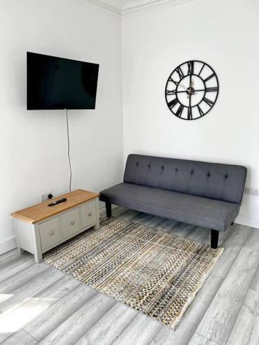 a living room with a couch and a clock on the wall at Luton flat with parking in Luton