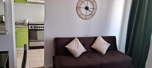 a couch with two pillows and a clock on a wall at Excelente departamento cerca del Movistar Arena in Santiago