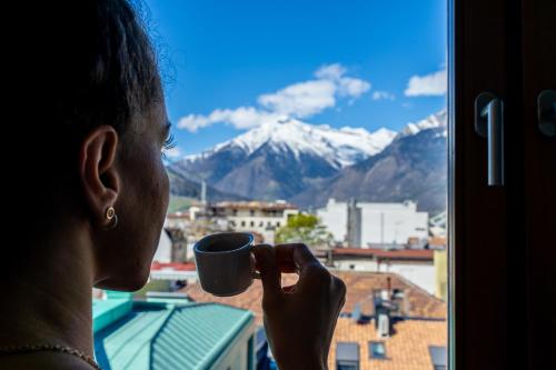 een vrouw met een kop koffie die uit een raam kijkt bij Ausblick Kleinjuwel mit Panoramablick + Garage in Merano