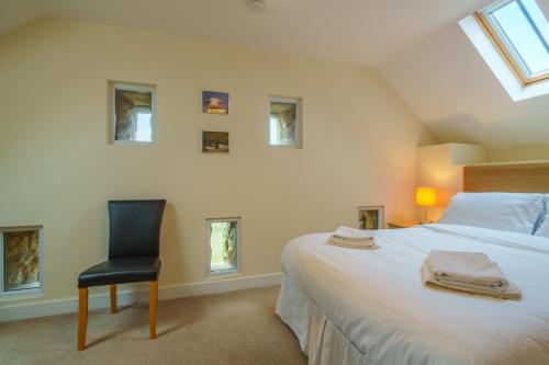 a bedroom with a bed and a chair and windows at 1 Peggies Barn - Rural cottage with great views in Maulds Meaburn