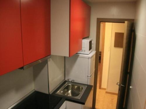 uma pequena cozinha com armários vermelhos e um lavatório em Hochwertige Ferienwohnung im Grüngürtel der Stadt em Madri