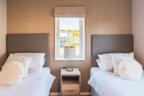 two beds with white pillows sitting next to a window at Luxurious 2-Bed Lodge in St Helens Ryde in Saint Helens