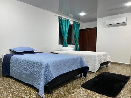 a bedroom with two beds and a window with blue curtains at HOTEL GANADERO in La Dorada