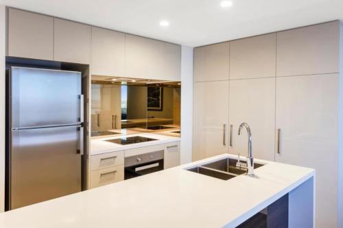La cuisine est équipée de placards blancs et d'un réfrigérateur en acier inoxydable. dans l'établissement Amazing 2BR delicate Apt, 1min to train station, à Brisbane