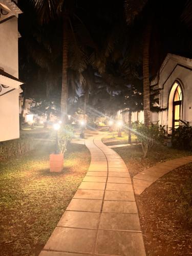 a walkway at night with palm trees and a building at Riviera Hermitage in Arpora