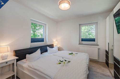ヘリングスドルフにあるVilla Doris Whg 4 Sonnenblickの白いベッドルーム(花の飾られたベッド2台付)