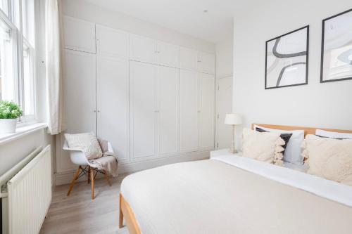 Heart of London's Holborn - CityApartmentStay في لندن: غرفة نوم بيضاء بسرير وكرسي