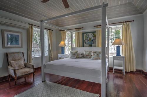 a bedroom with a bed and a chair and windows at La Hacienda Bellevue in Bridgetown