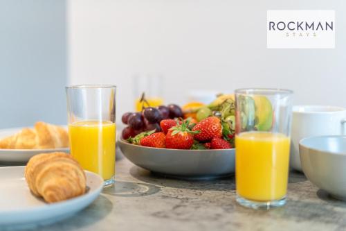 a table with a bowl of fruit and two glasses of orange juice at Royal Oak 1 - FREE PARKING - 2 Bedroom Apartment - 2 bathrooms - Sleeps 6 - Perfect for Contractors - Fast Wi-fi in Brentwood