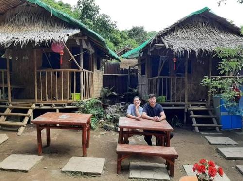 a man and woman sitting at a picnic table in front of buildings at YOUMEBED MOTOR INN at Kambal Kubo Resthouse in Antipolo