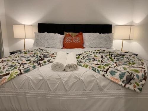 a large bed with two towels and two lamps at Brand New Entire 4 Bed House Multiple Free Parking Early Check-in Late Check- Out Allowed in South Ockendon