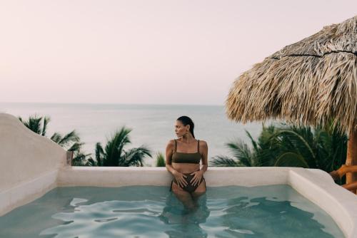 a woman in a bikini sitting next to a swimming pool at Casa Las Tortugas Petit Beach Hotel & Spa in Holbox Island