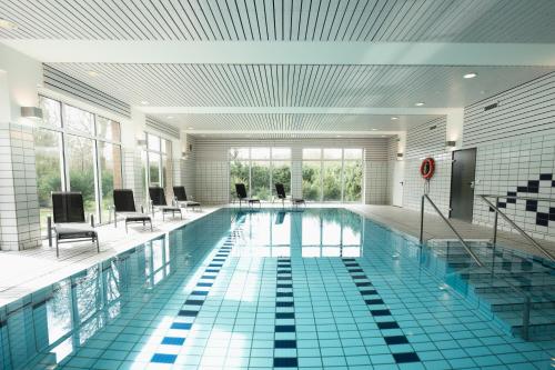 a large swimming pool with chairs and tables in a building at Hotel am Park Bad Driburg in Bad Driburg