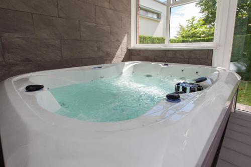 a large white bath tub with a window at Luxe Arthurs Seat View Townhouse with Hot Tub in Edinburgh