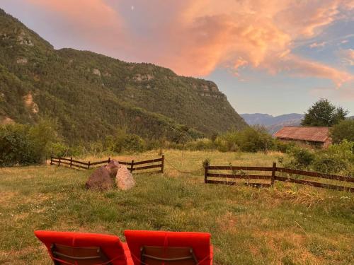 two red chairs in a field with a fence and mountains at Maison Gaia in Valdeblore