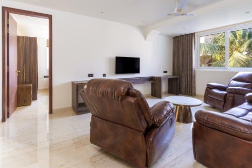 a living room with two leather chairs and a television at The Tanisi Hotels and Resorts, Candolim in Candolim