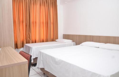 a hotel room with two beds and an orange curtain at Hotel Manoá Poa - Uma quadra do complexo da Santa Casa in Porto Alegre