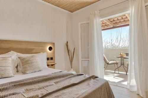 a white bedroom with a bed and a balcony at Santa Maroma Rooms & Houses in Vasilikos