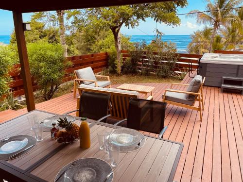 une terrasse en bois avec une table et des chaises et l'océan dans l'établissement Bungalow Jacuzzi - Pieds dans l'eau, à Trois Bassins