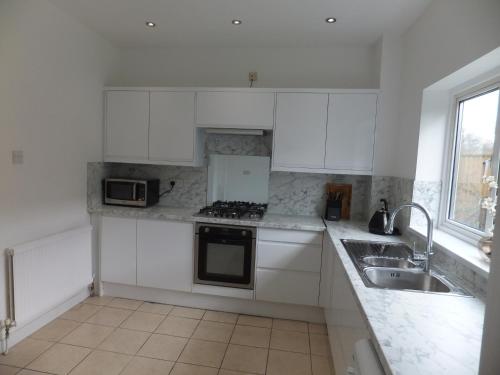 a white kitchen with white cabinets and a sink at Many Worlds Meet - EuroStar, Wimbledon 30 mins, Central London, Gatwick 15 mins - Spacious, Sleeps up to 16 plus Cot - Free WiFi, Parking - Next to Lloyd Park, Great for Families, Walkers, Relocators - Ideal for Contractors in Croydon