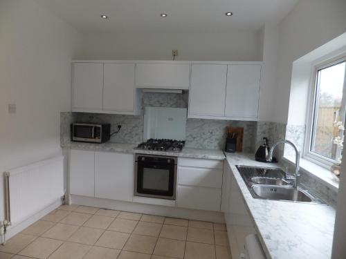 a white kitchen with white cabinets and a sink at 15 mins from East Croydon to Central London, Gatwick - Sleeps up to 7 couples plus Babies - Free WiFi, Parking - Next to Lloyd Park, Great for Walkers - Ideal for Contractors - Families - Relocators in Croydon