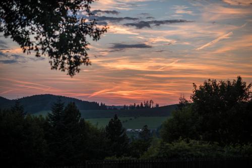 a sunset over a field with trees and mountains at Ferienhäuser Hoher Knochen in Winterberg