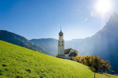 Una iglesia en una colina verde con el sol detrás. en Ferienwohnung in den Dolomiten mit traumhafter Aussicht, en Kastelruth