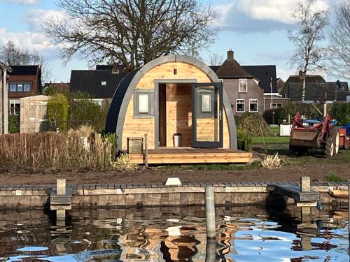 Une petite maison est assise à côté d'un étang dans l'établissement Camping pod Tiny House aan het water, à Belt-Schutsloot