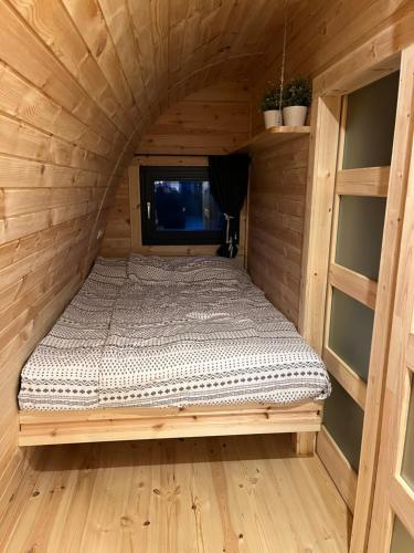 a bed in a wooden cabin with a window at Camping pod Tiny House aan het water in Belt-Schutsloot