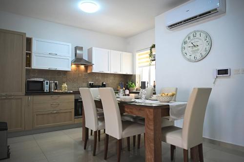 a kitchen with a table with chairs and a clock on the wall at Fl 2 Ta'lonza Luxury With Hot Tub By Homely in Mellieħa