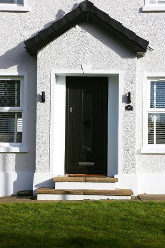 a black door on a white house with grass at Newly refurbished home on the North Coast - AONB in Bushmills